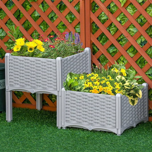 Two grey rattan-effect planters filled with yellow and purple flowers, set on grass in front of a wooden fence