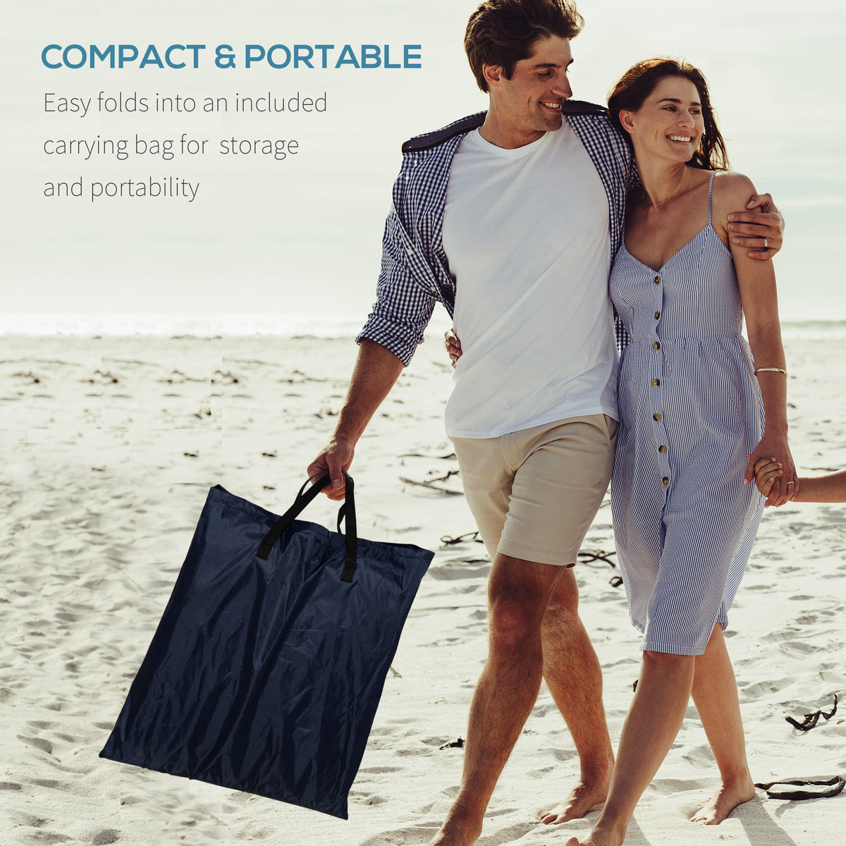 A couple walking on the beach carrying the folded beach gear in a dark blue storage bag