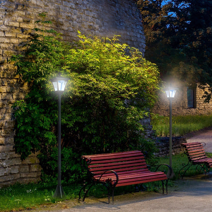 Two solar post lamps illuminating a garden path next to a stone wall and benches