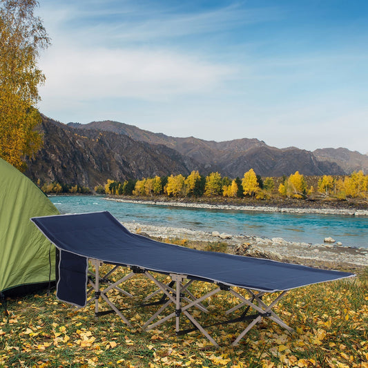 The camping cot placed on a grassy riverbank next to a green tent in a scenic outdoor setting