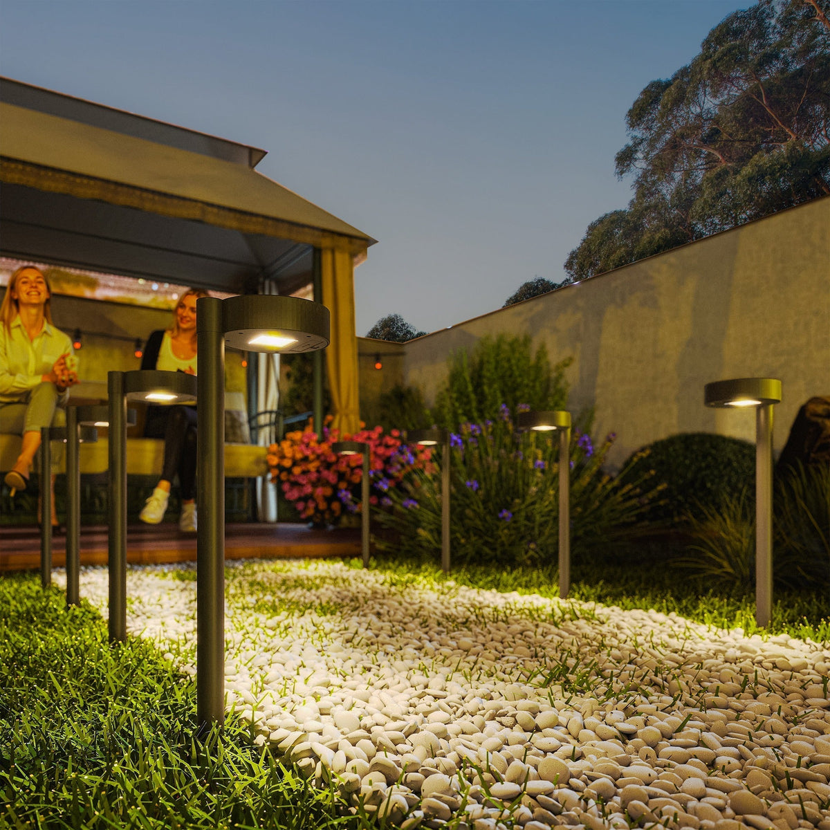 The garden lighting illuminating a pebble pathway in a backyard at night with people sitting nearby