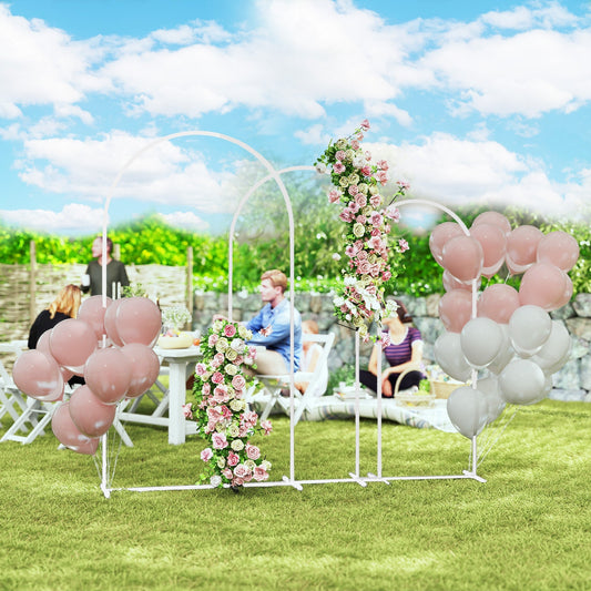A white metal balloon arch stand set decorated with pink and white balloons and flowers at an outdoor party