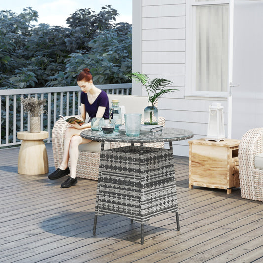 The rattan garden table is shown on a patio with a woman sitting nearby reading a book