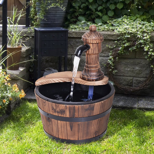 A wooden barrel water fountain with a pump and spout, set up in a garden on a patio