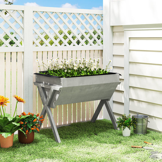The elevated planter box filled with white flowers standing on a lawn against a garden fence