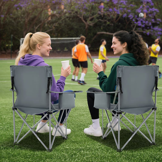 Two women sitting on grey camping chairs at a sports field