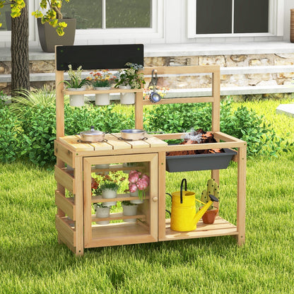 The play kitchen set placed on a green lawn in front of a house with a stone wall and garden plants