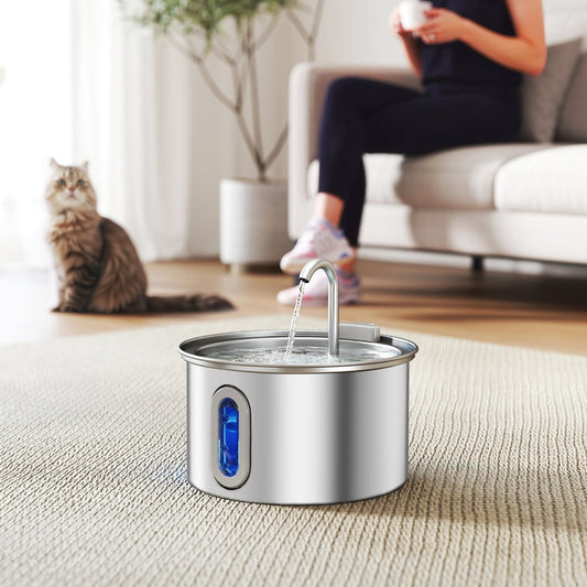 Stainless steel cat water fountain in use with a cat drinking and a person sitting on a sofa