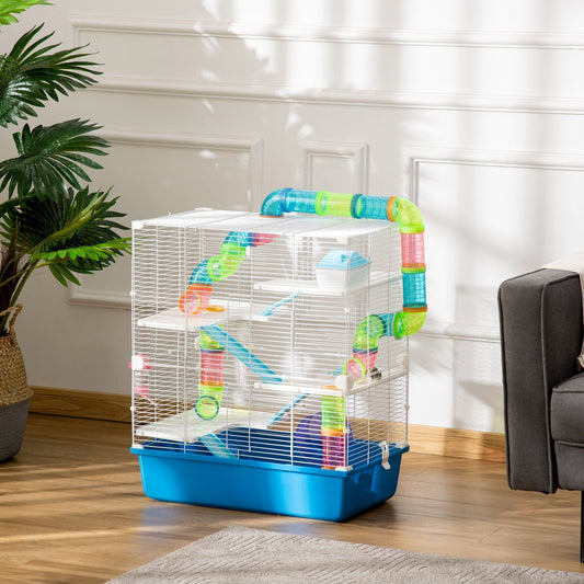 The hamster cage set up in a living room with a sofa and plant nearby