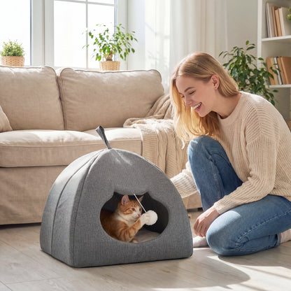A woman playing with a kitten inside the grey cat house bed in a living room