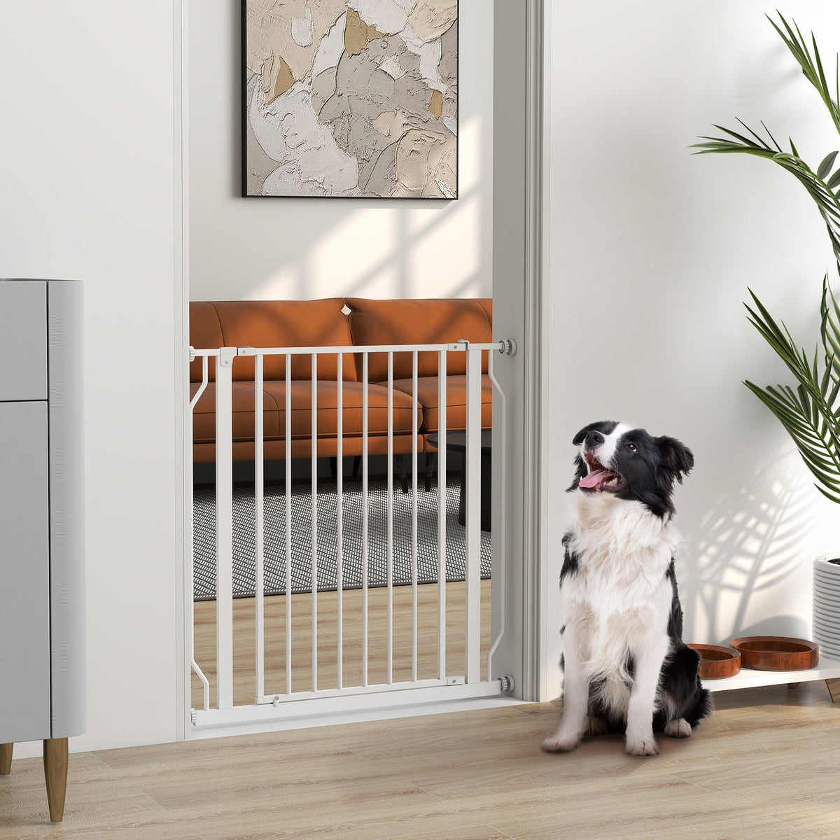 A white metal dog gate installed in a doorway with a black and white dog sitting in front of it