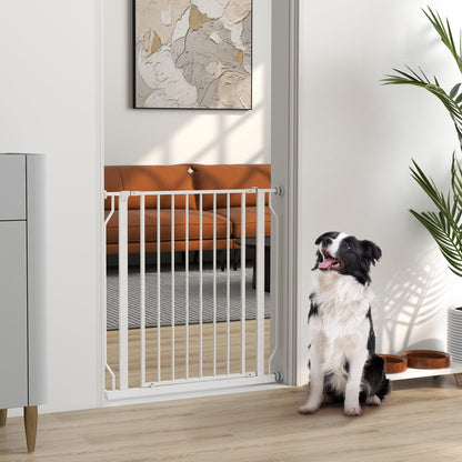 A white metal dog gate installed in a doorway with a black and white dog sitting in front of it