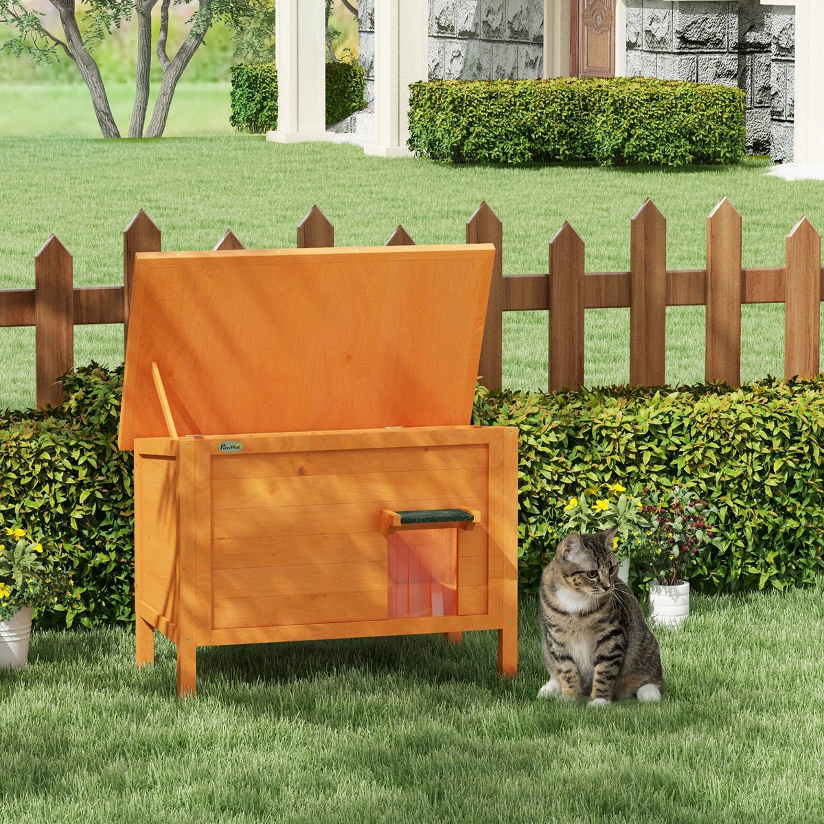 The cat house standing on a green lawn with its roof propped open and a cat sitting nearby