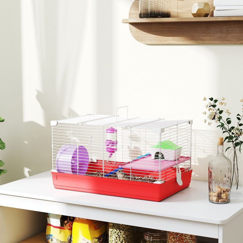 The hamster hutch is set up on a white table with some bags of pet food underneath