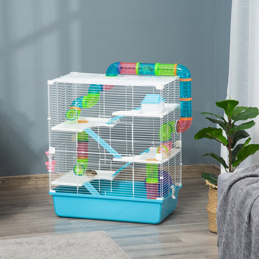 The hamster cage placed in a living room next to a green plant and a grey sofa