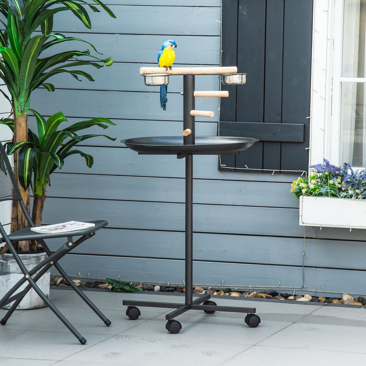 The bird feeder station with a parrot perched on a wooden dowel, set on a patio