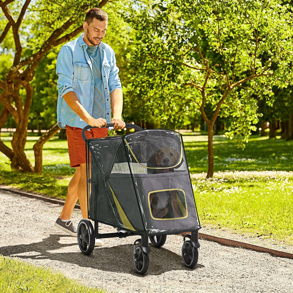 Man pushing the grey pet travel stroller with a dog inside through a park