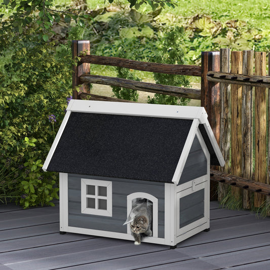 the outdoor cat shelter, a grey wooden feral cat house with a pitched asphalt roof, shown on a wooden deck