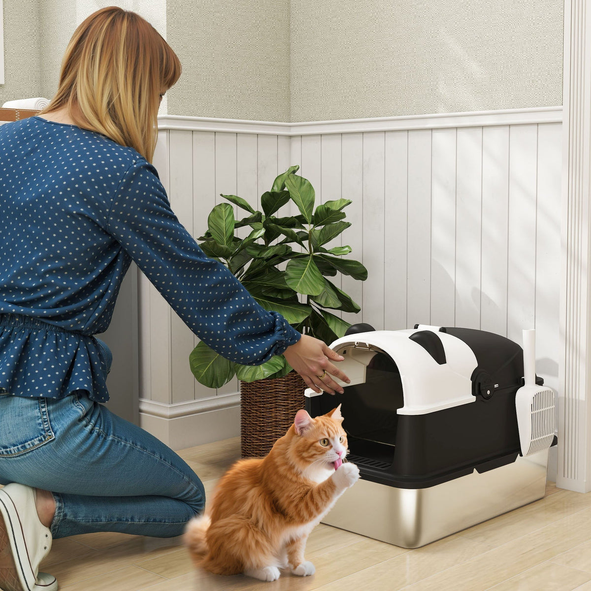 A woman placing a ginger cat into the enclosed panda style litter box in a bright room