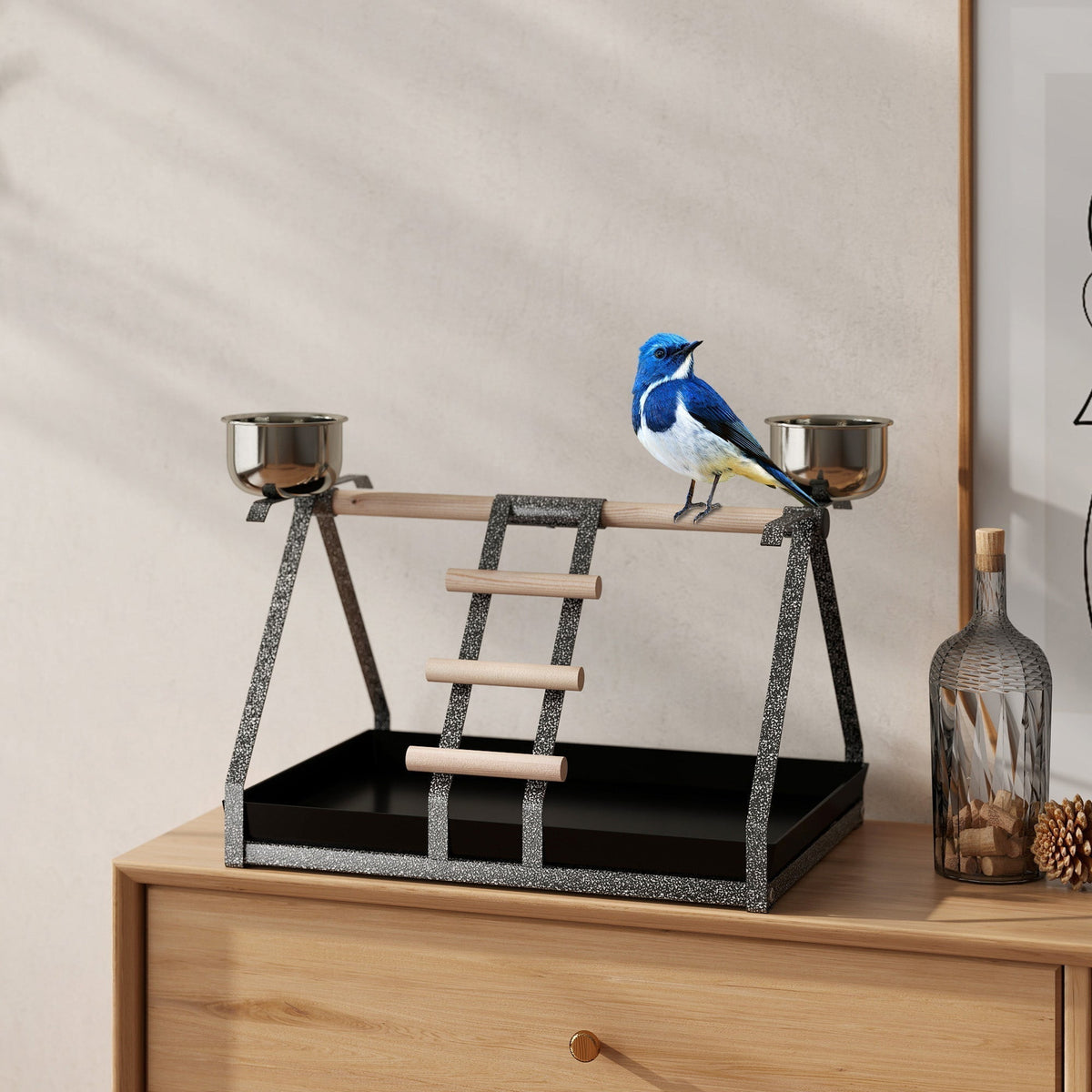 The bird stand is placed on a wooden dresser next to a bottle and a picture frame