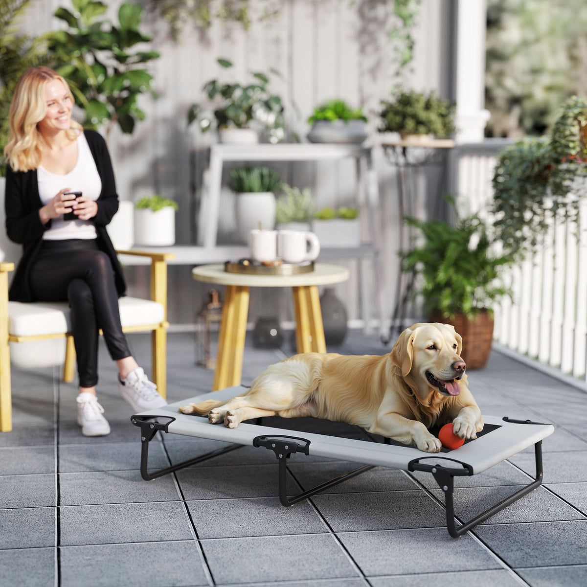 The elevated dog bed placed on a patio with a golden retriever lying on it playing with a ball