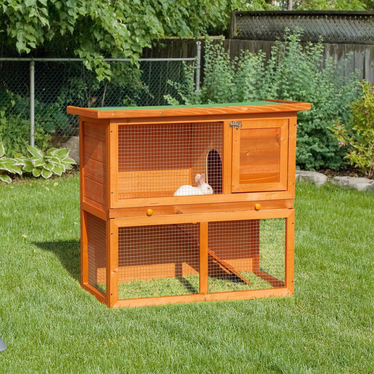 The wooden pet cage placed on a green lawn with a small white rabbit inside