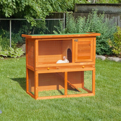 The wooden pet cage placed on a green lawn with a small white rabbit inside