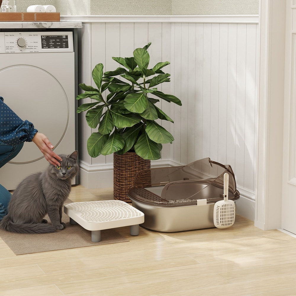The stainless steel litter box placed on a floor next to a cat and a green houseplant