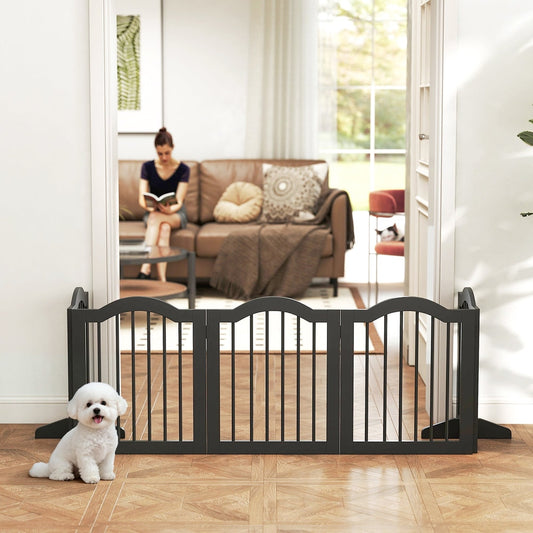 The black wooden dog gate is set up in a doorway with a small white dog sitting in front of it