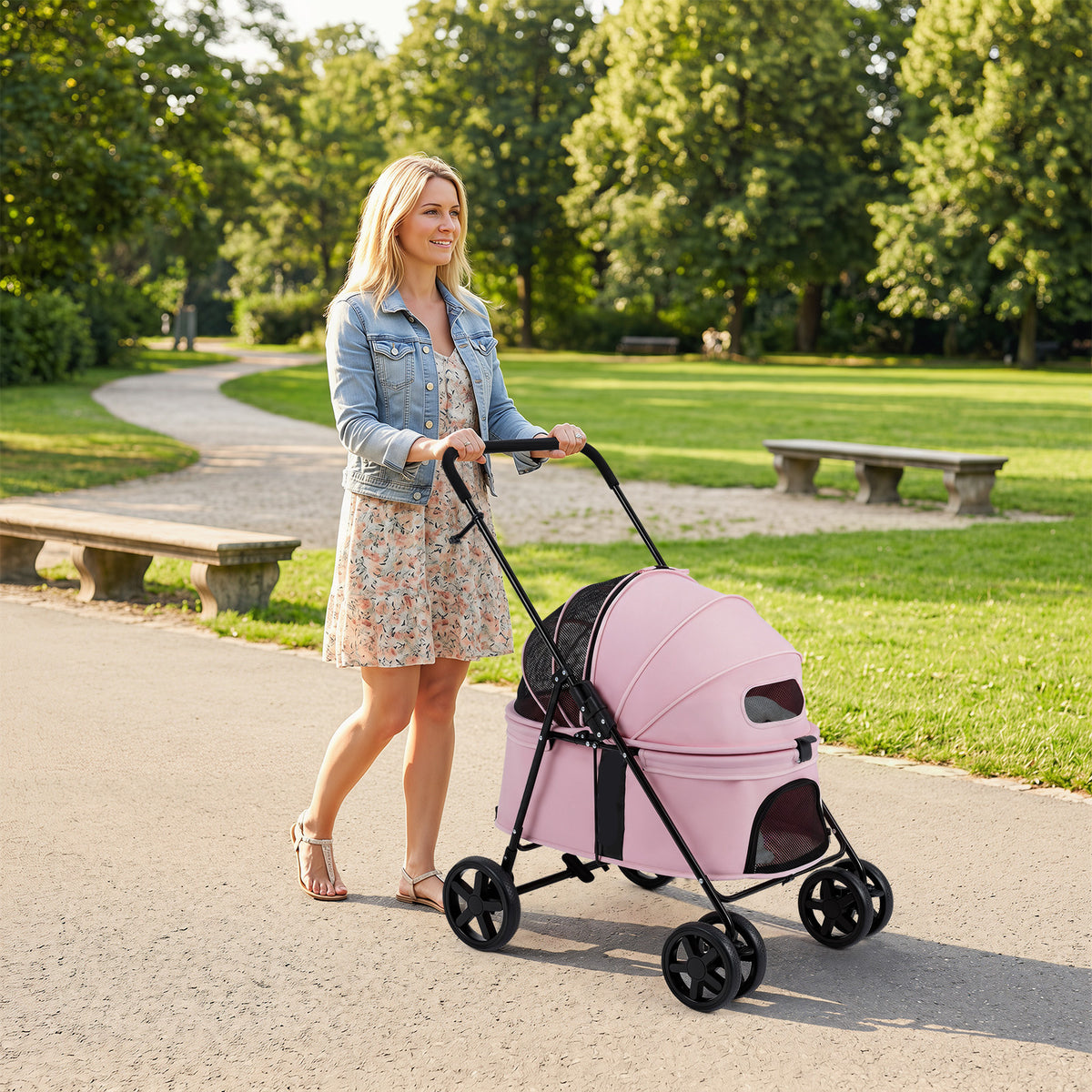 The dog stroller being pushed by a woman along a path in a green park