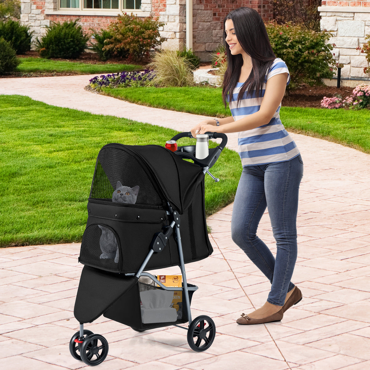 Woman pushing the black pet stroller with a cat inside on a paved garden path