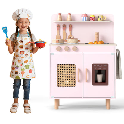 A child in an apron holds a toy pot next to the pink play kitchen