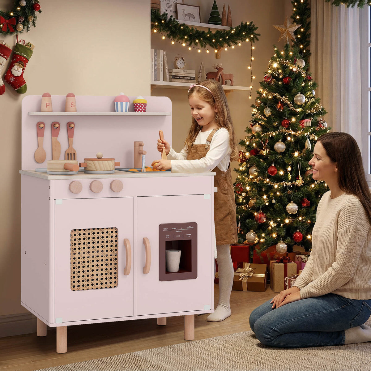A mother and child play with the pink toy kitchen near a Christmas tree