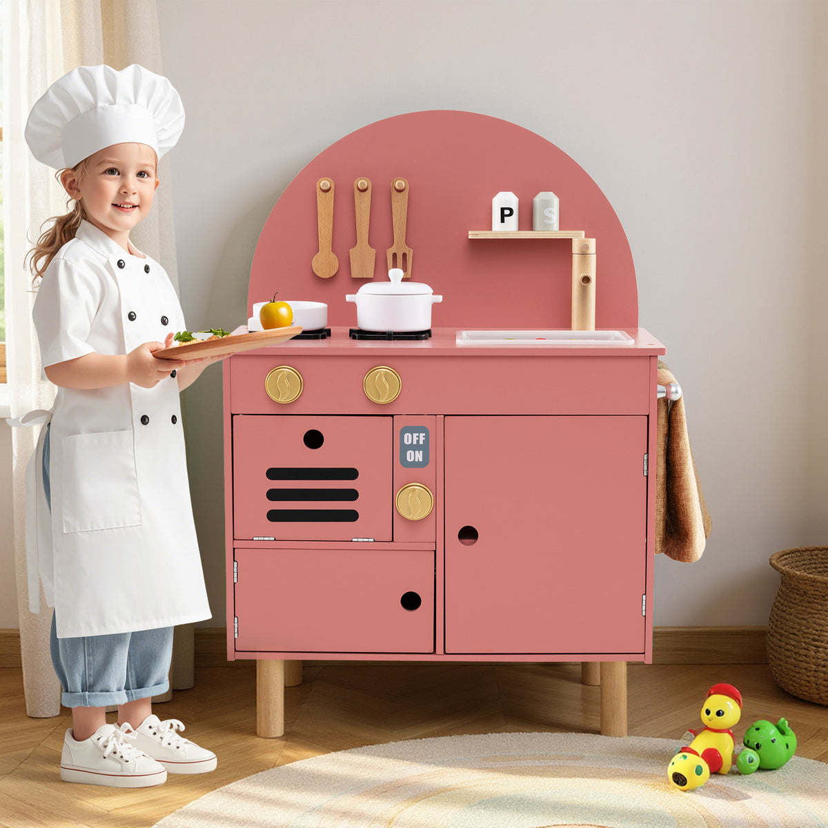 A child in a chef's hat plays with the pink wooden kitchen set