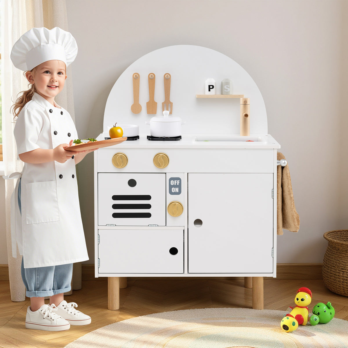 A young girl in a chef's hat and apron stands by the wooden play kitchen