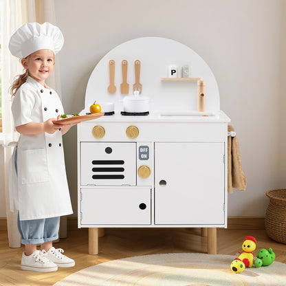 A young girl in a chef's hat and apron stands by the wooden play kitchen