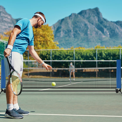 The blue badminton net set up on a court with a man about to hit a tennis ball