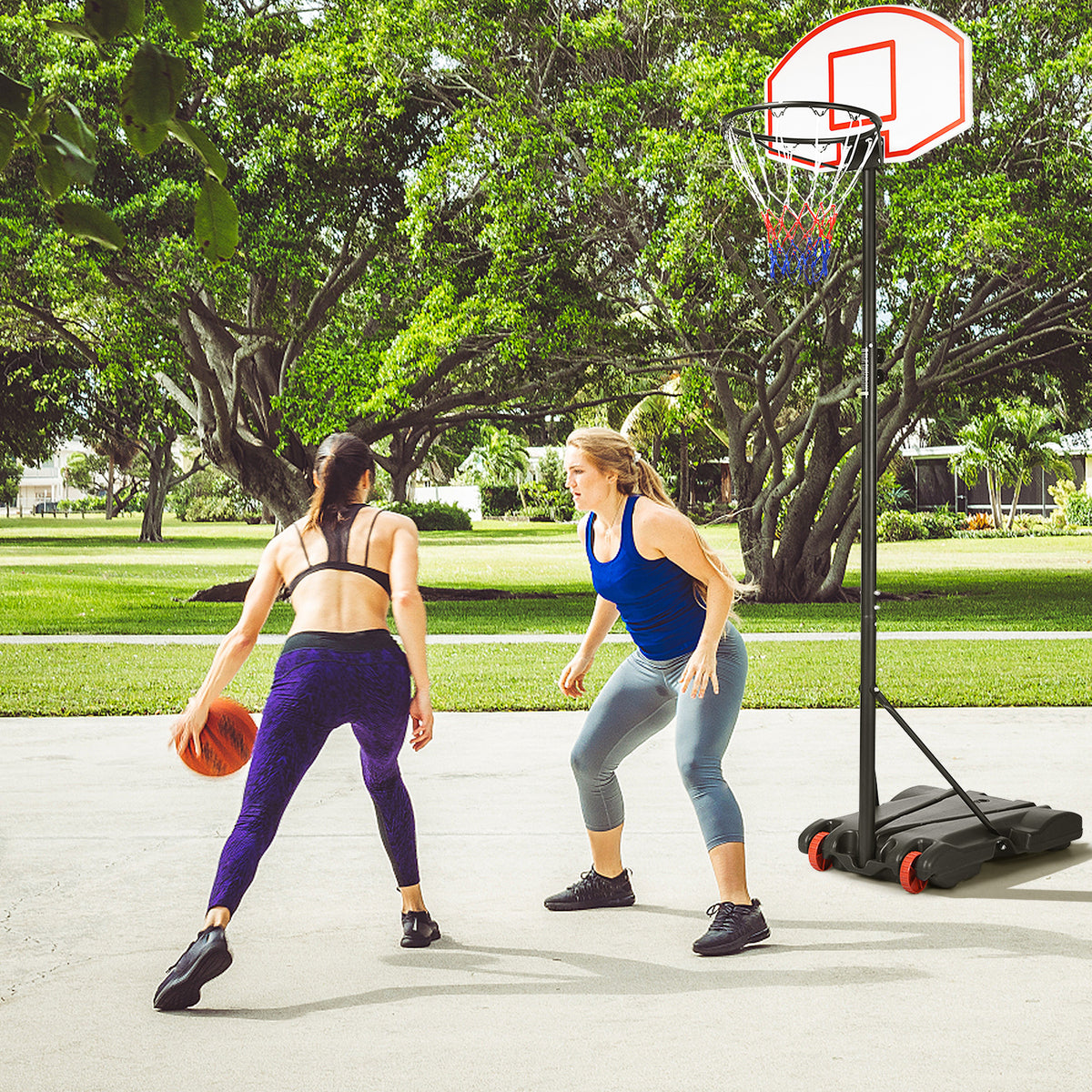 Two women playing basketball with a portable hoop in a park setting