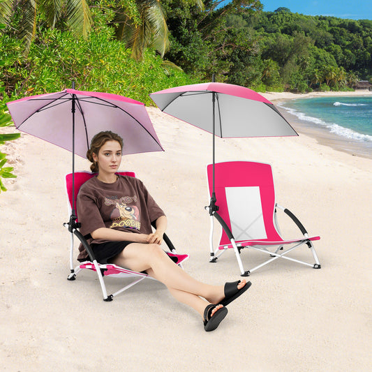 A woman sits on the pink beach chair with parasol on a sandy beach, another chair is nearby