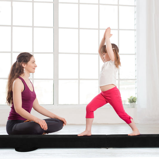 The gymnastic beam being used by a young girl in a bright room while a woman watches