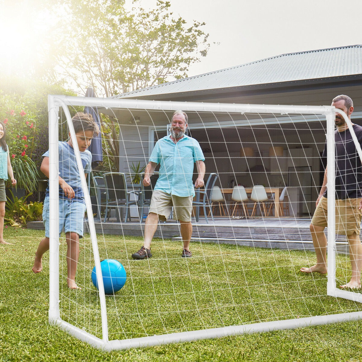 The soccer goal set up on a grassy lawn with a family playing a game together