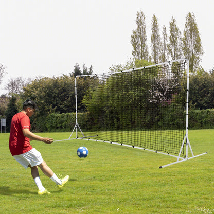 Man in a red football kit kicking a ball towards the rebounder net on a grass field