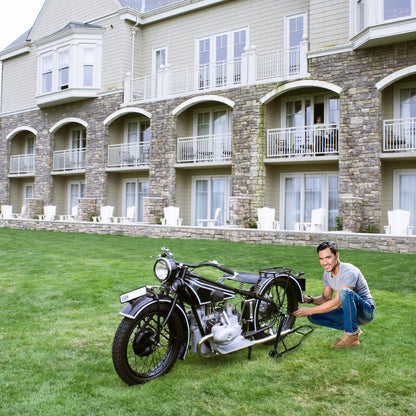 A man placing a vintage motorcycle onto the black rear wheel lift stand on grass