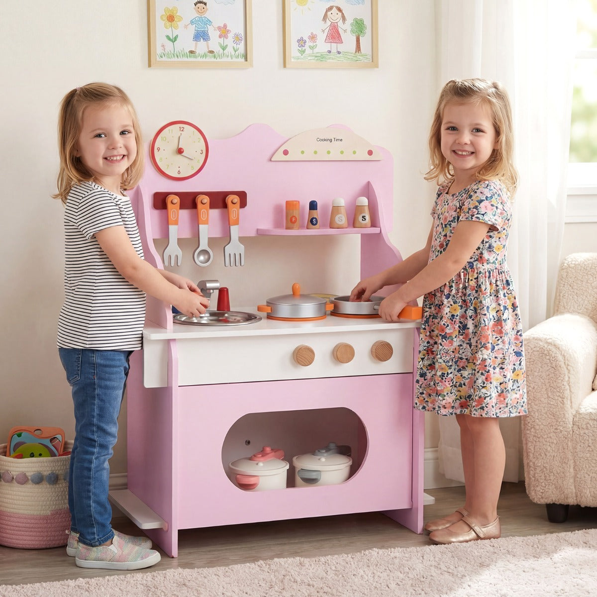 Two young girls standing and playing with the pink play kitchen set in a bright living room