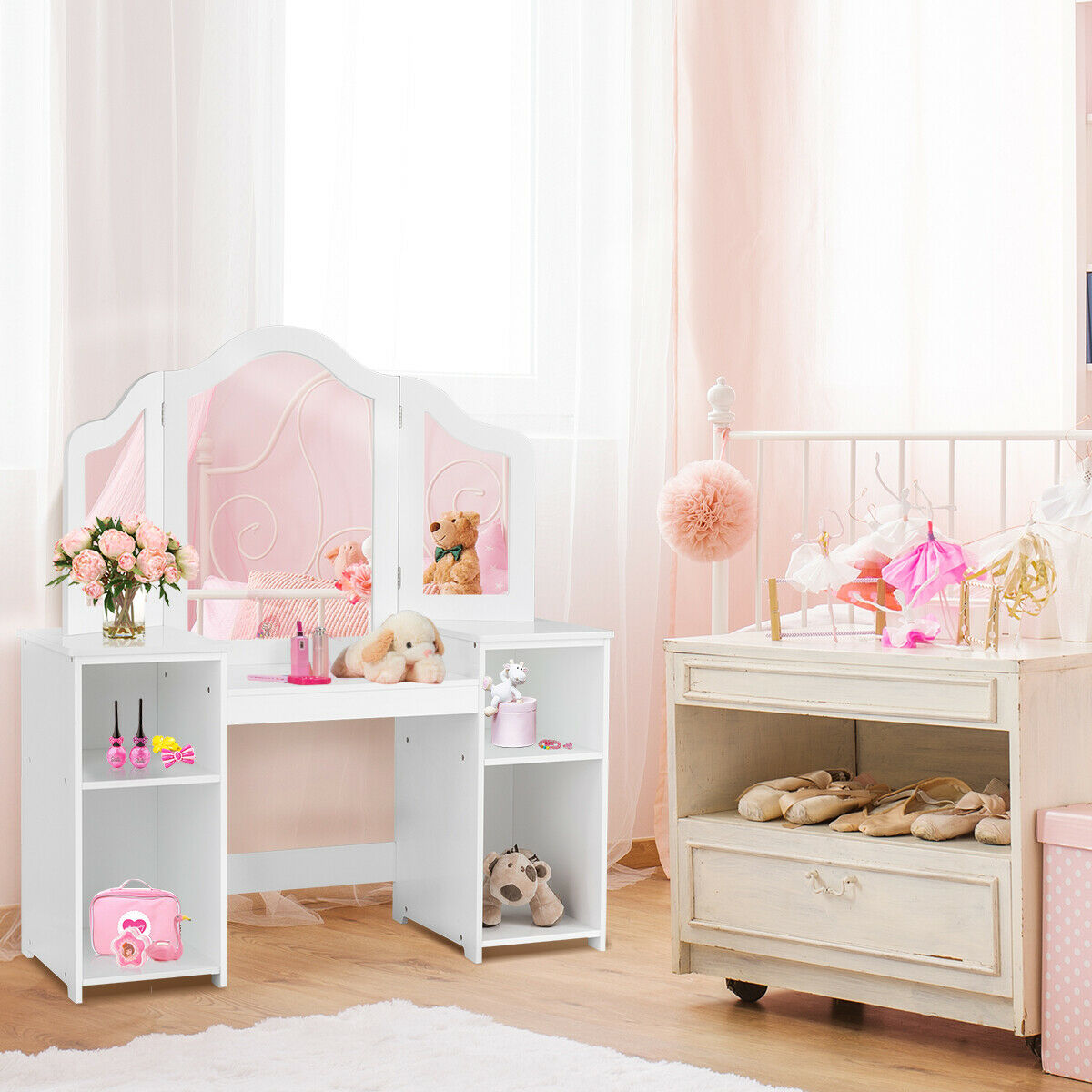 A white kids vanity table with a triple mirror is set up in a pastel pink bedroom