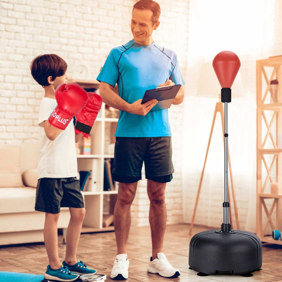 A boy in red boxing gloves trains with a punching bag and stand, supervised by a man