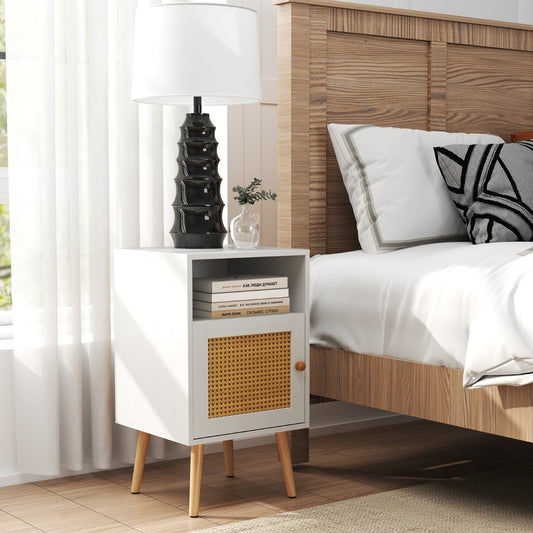 The white bedside cabinet with a woven door panel standing beside a wooden bed frame
