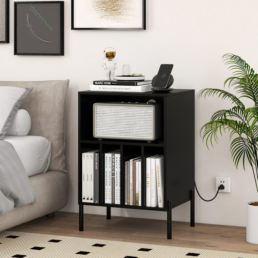 The record player stand in a bedroom next to a bed, holding books and a charging phone