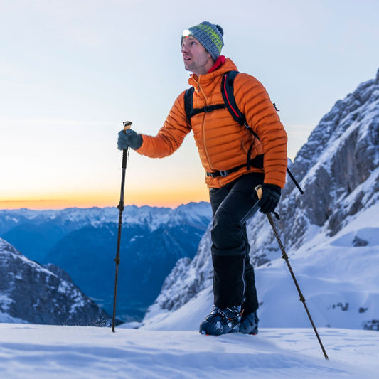 Man wearing ski gear uses the black hiking poles while walking on snow
