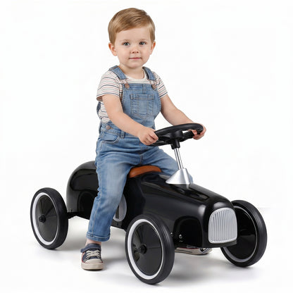 A young boy sits on the black push and pedal ride on toy, looking at the camera